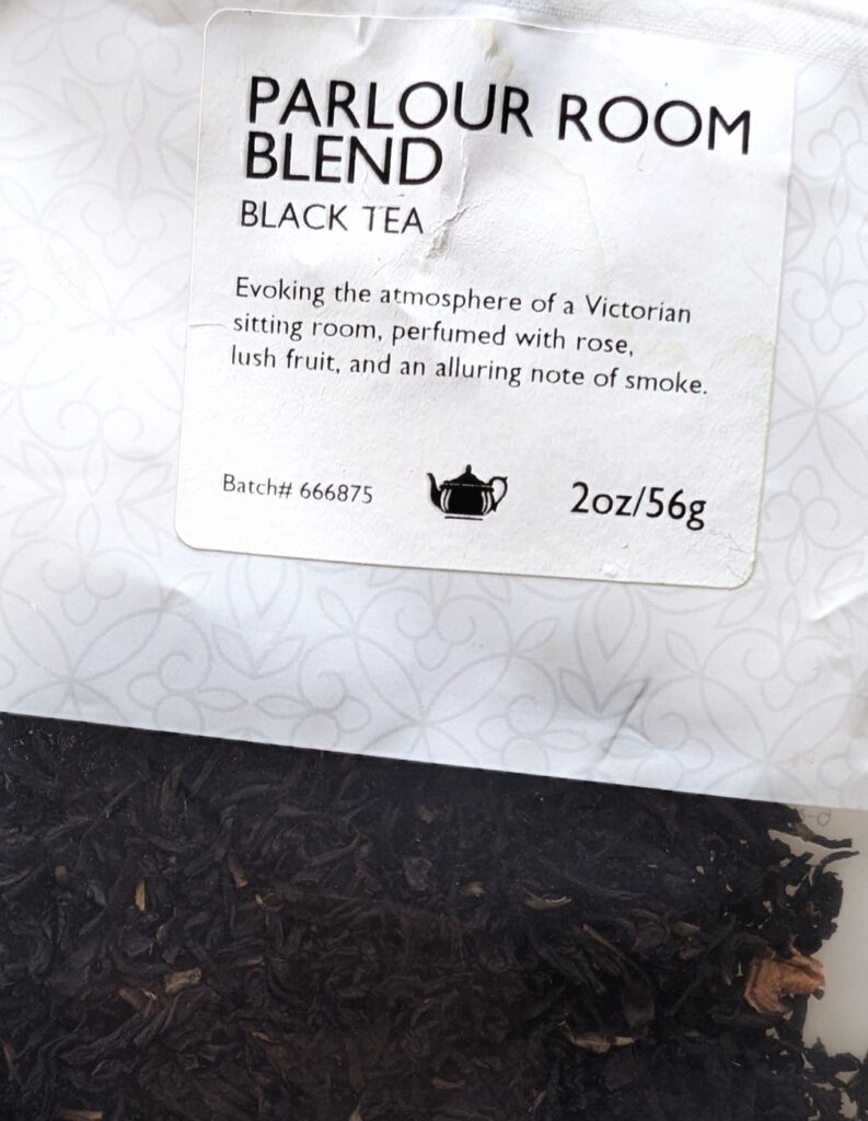 Photo of a tea label that reads: Parlour Room Blend. Black Tea. Evoking the atmosphere of a Victorian sitting room, perfumed with rose, lush fruit, and an alluring note of smoke. 2oz/56g