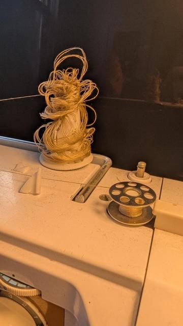 Photo of the top of a sewing machine in the process of loading thread onto a bobbin. The bobbin is fine but the spool of thread has collapsed and has a fountain of knotted loops at the top