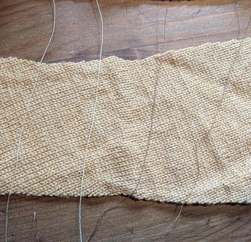 Close photo of four different beige and tan threads trailing across a piece of mustard yellow fabric