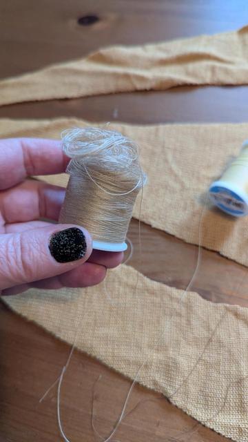 Close photo of my hand holding a spool that is normal at the bottom but devolves into a loose mass of threads at the top
